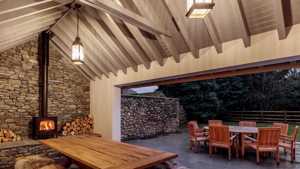 A stone fireplace with a wood-burning stove, a wooden dining table, and outdoor seating with chairs.