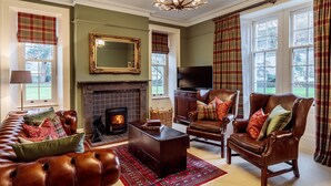 A cozy living room with a fireplace, leather furniture, and plaid curtains.