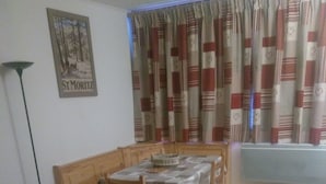 Ruokailutila, jossa on pöytä ja tuolit, punainen sohva, lattiavalaisin ja ikkuna, jossa on verhot.