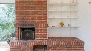 A brick fireplace with a metal screen, white shelves above, and a potted plant on the middle shelf. - Vacation home Heidehaus for up to 6 people (Enge-Sande)