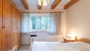 A bedroom with a wooden wardrobe, a bed, a window with curtains, a bedside lamp, and a heater. - Vacation home Heidehaus for up to 6 people (Enge-Sande)