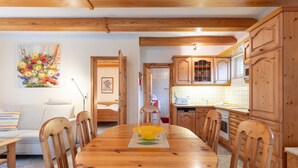 A wooden dining table with chairs, a kitchen with wooden cabinets, and a painting on the wall. - Vacation home Heidehaus for up to 6 people (Enge-Sande)