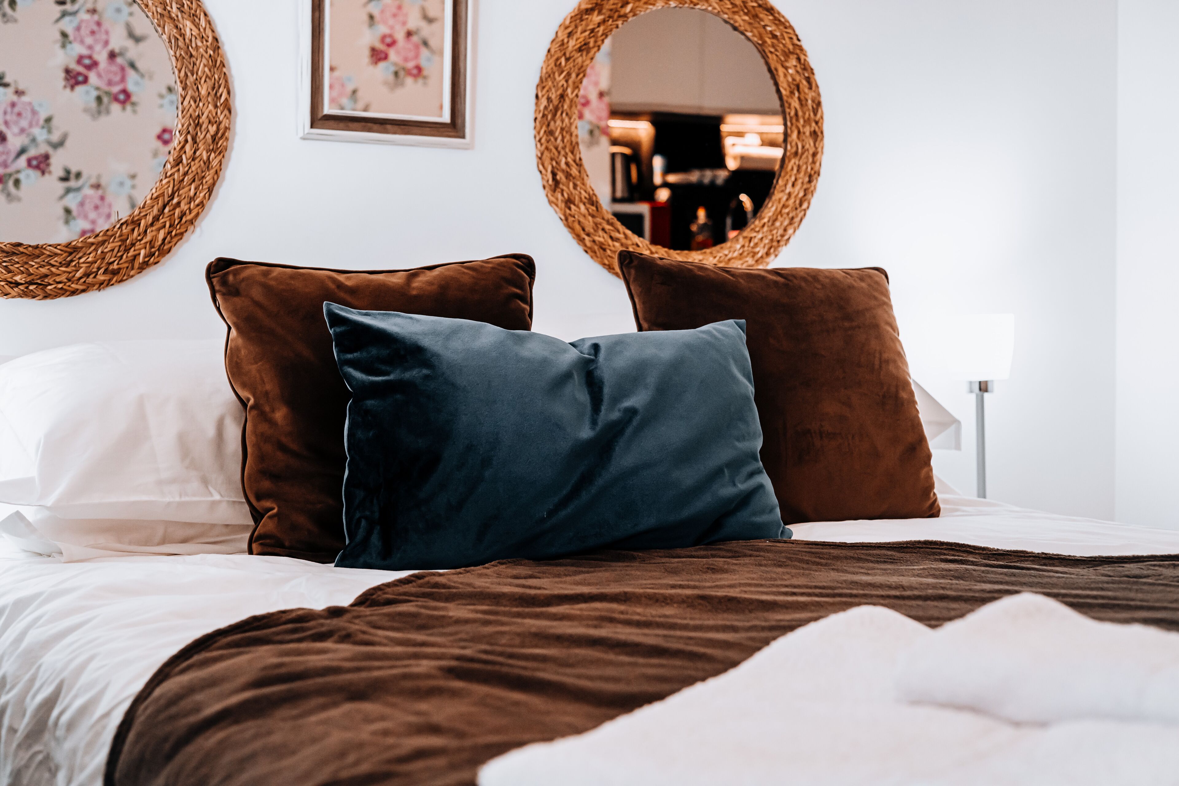 A neatly made bed with brown and white bedding, two brown pillows, and a blue pillow.