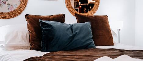 A neatly made bed with brown and white bedding, two brown pillows, and a blue pillow.