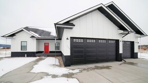 Ein modernes, zweistöckiges Haus mit roter Tür, einer Garage mit mehreren Toren und einer überdachten Auffahrt.