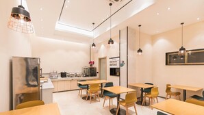 A modern dining area with wooden tables and chairs, pendant lighting, and a kitchen area with appliances. - City Comfort Inn (Guangzhou)