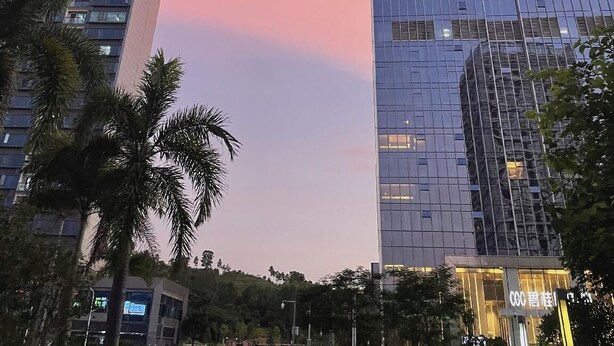 A tall, modern skyscraper with reflective glass windows and a pinkish sky in the background. - City Comfort Inn (Guangzhou)