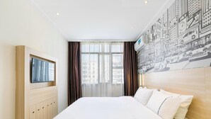 A hotel room with a bed, a TV mounted on a wooden cabinet, a large window with curtains, and a cityscape mural on the wall. - City Comfort Inn (Guangzhou)