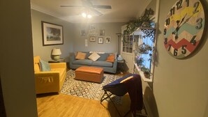 A living room with a sofa, a yellow armchair, a patterned rug, a ceiling fan, and a wall clock. - Built in 1866 this hillside home is close to everything! (Duluth)