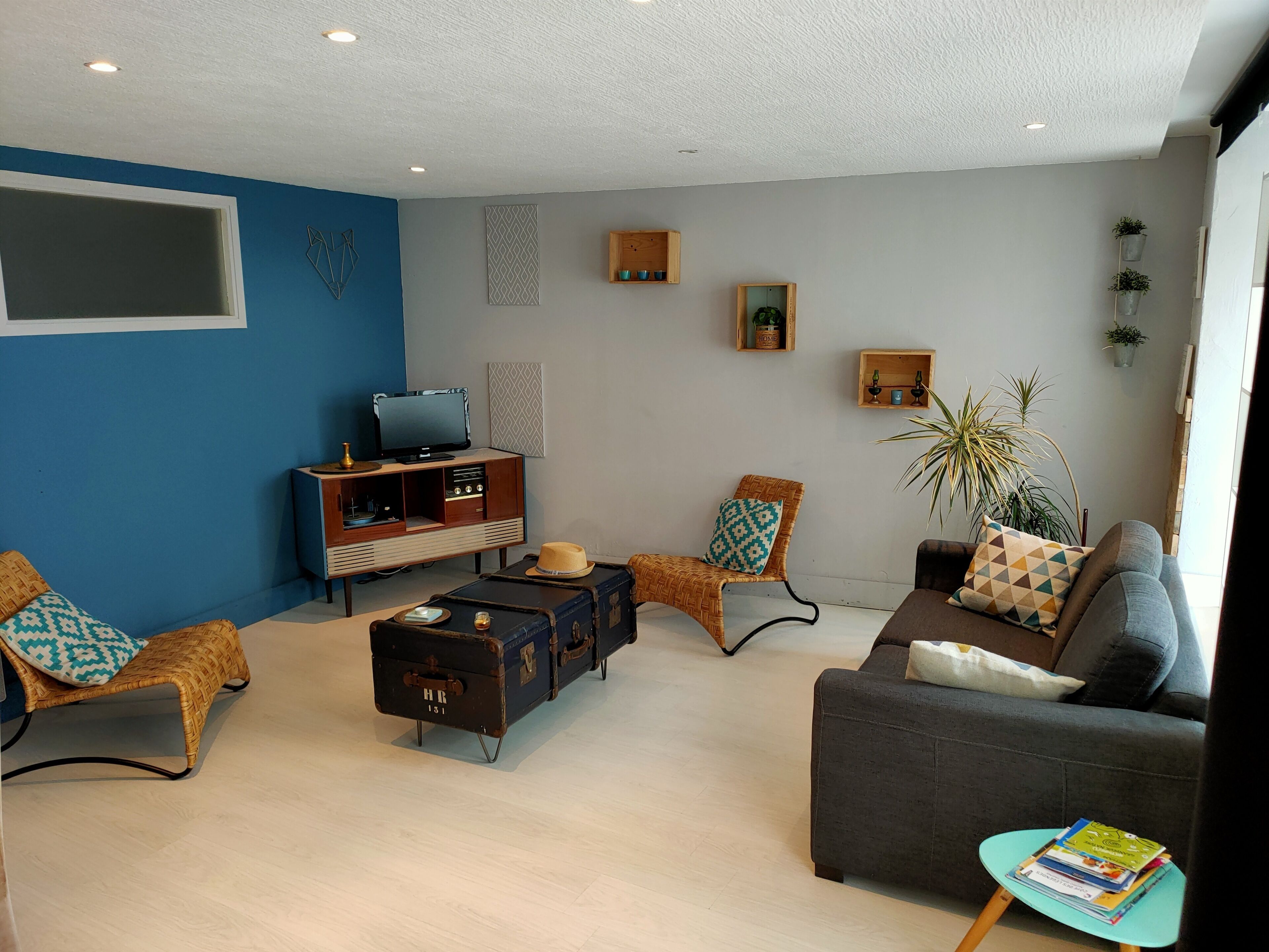 A living room with a blue accent wall, a vintage TV, a bookshelf, a sofa, a coffee table, and a small side table with books.