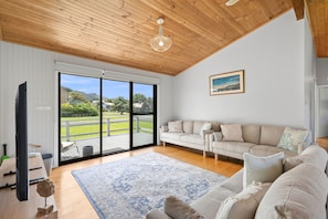A spacious living room with a large sliding glass door leading to a deck, a flat-screen TV, a wooden ceiling, and a painting on the wall. - Shell Shack (Apollo Bay)