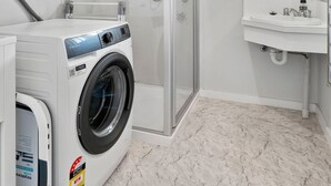 A laundry room with a front-loading washing machine, a glass-enclosed shower, and a window.