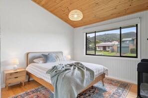 A bedroom with a bed, bedside lamps, a window with a view, and a ceiling light fixture. - Shell Shack (Apollo Bay)