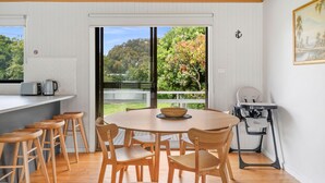 A dining area with a round table, wooden chairs, and a view of a garden through a glass door.