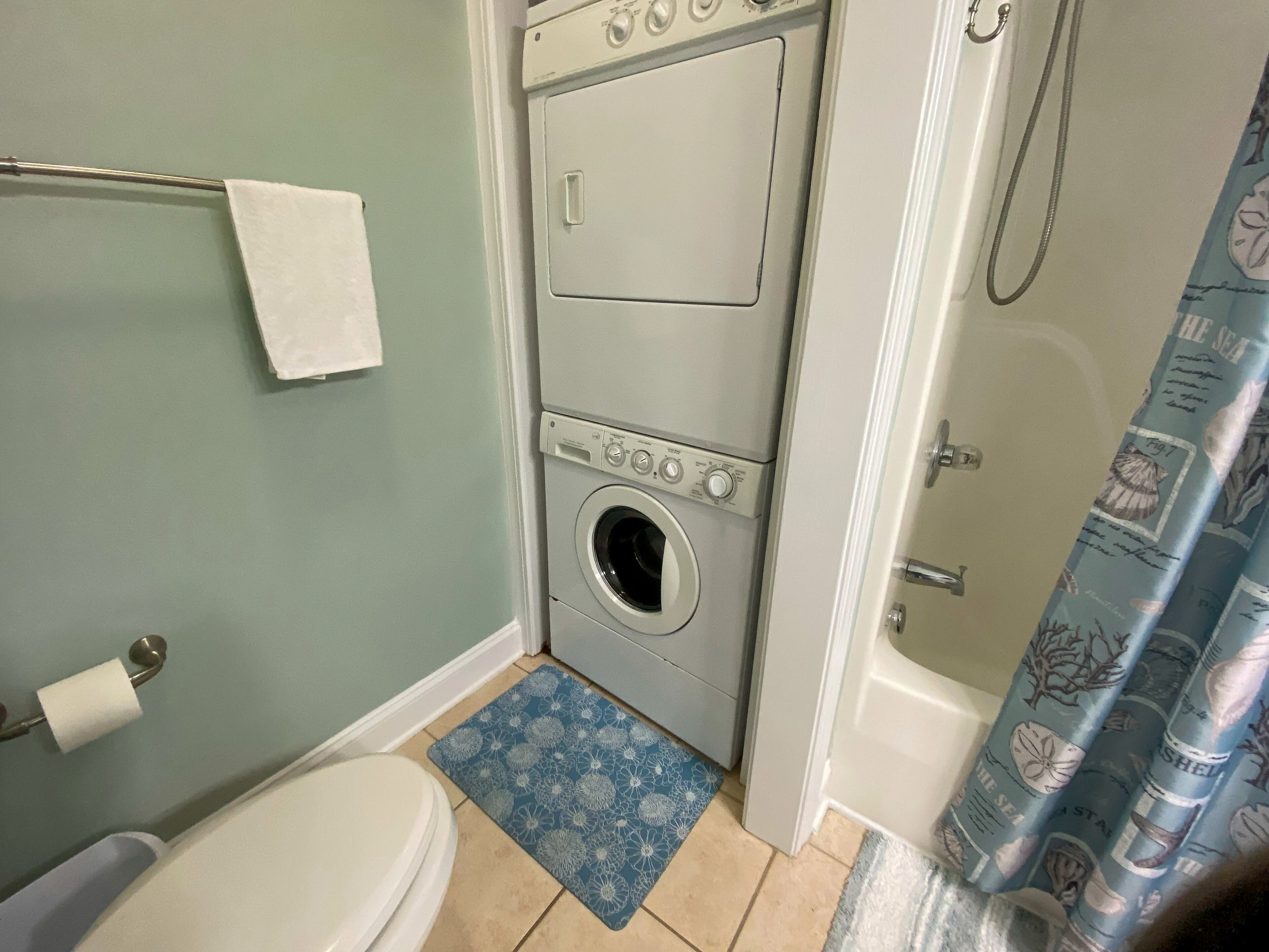 A compact bathroom with a toilet, a washing machine, and a shower curtain.