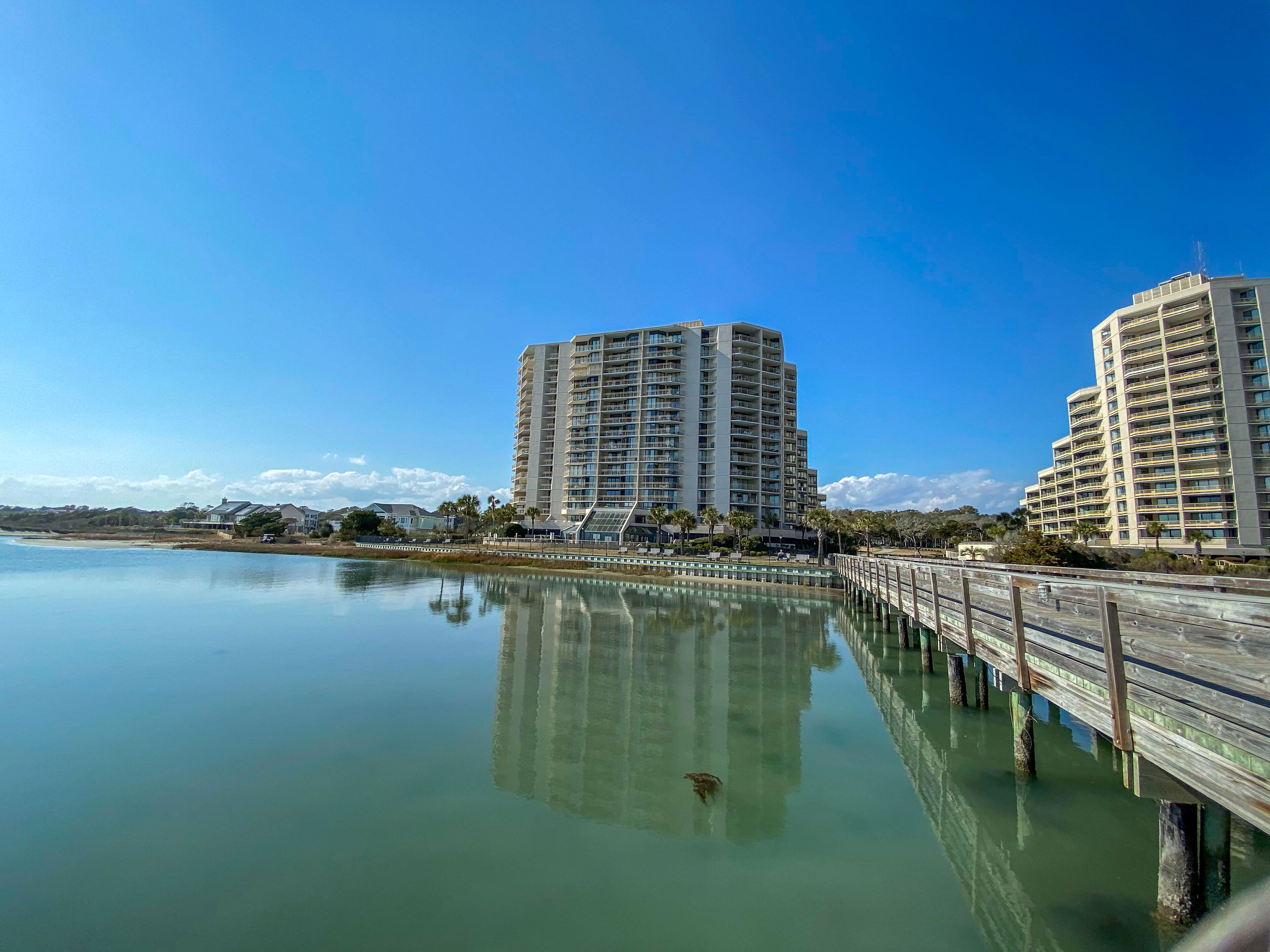 A waterfront view with two high-rise buildings, a calm body of water, and a wooden pier.