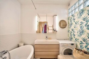 Un baño con bañera, lavabo con espejo, lavadora y perchero.