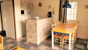 Ett kompakt kök med en köksö i mitten, ett matbord med stolar och ett fönster med gardiner.