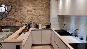 A modern kitchen with white cabinets, a stone wall, and a wooden countertop.