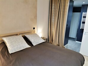 Une chambre à coucher avec un lit, deux oreillers, une table de chevet, une lampe et une vue sur la salle de bain.