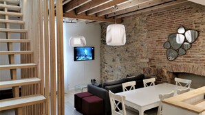 A modern living room with a brick wall, a flat-screen TV, a fireplace, and a dining area with a white table and chairs.