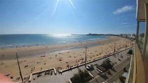 A beach with a long promenade, a pier in the distance, and buildings along the coastline.