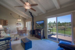 Ein geräumiges Wohnzimmer mit Deckenventilator, Kamin, Fernseher und einem Balkon mit Ausblick ins Freie.