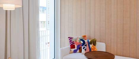 Un salon moderne avec un canapé blanc, des coussins colorés, une petite table en bois et une grande fenêtre avec des rideaux.