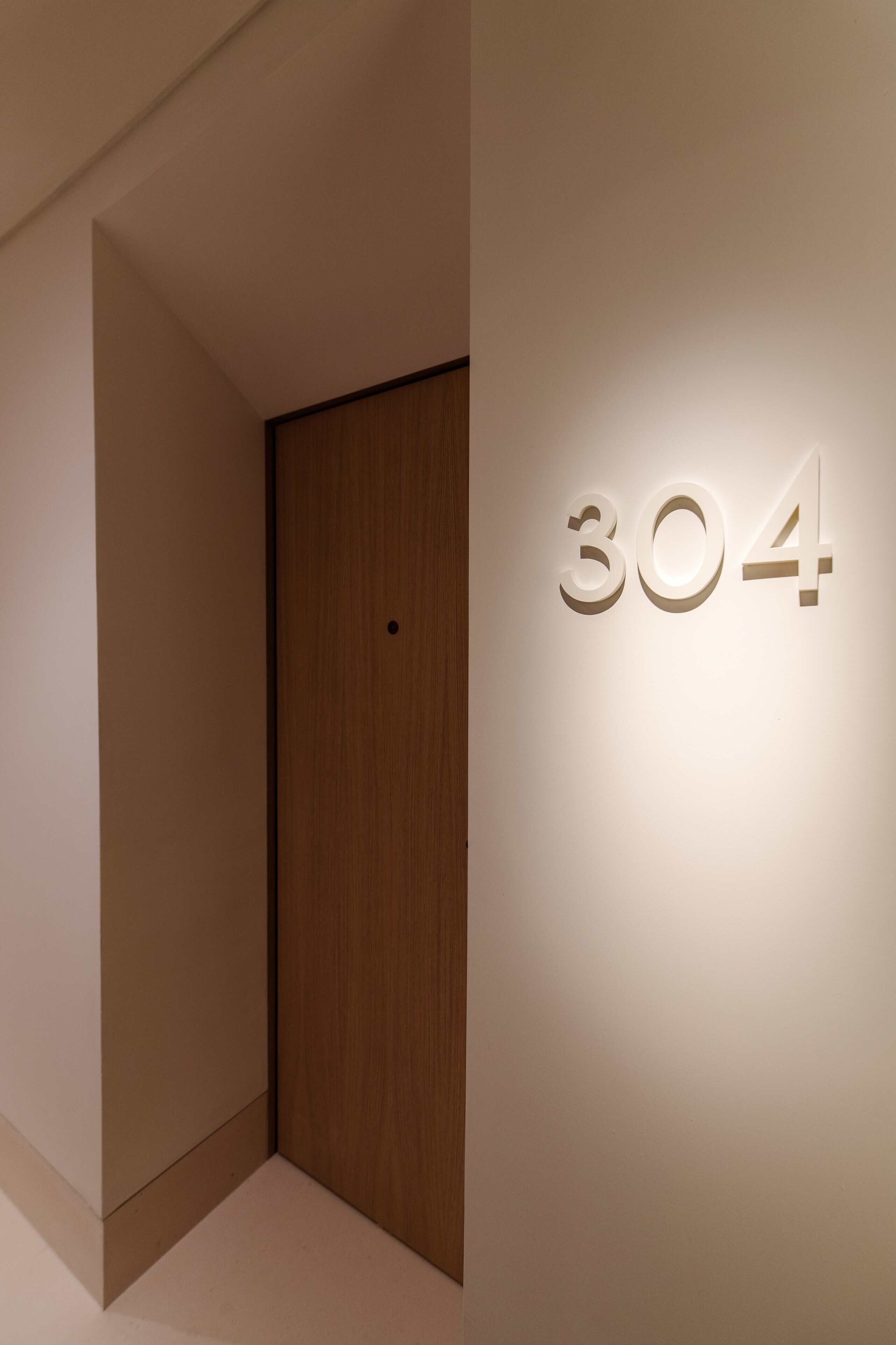 Ein Korridor mit einer Holztür und einer Wand, auf der die Nummer „304“ angebracht ist.