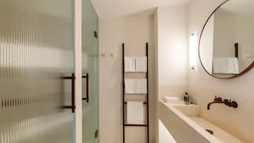 Une salle de bain moderne avec une douche à parois de verre, une échelle en bois pour suspendre les serviettes, un grand miroir et un lavabo beige avec un robinet.