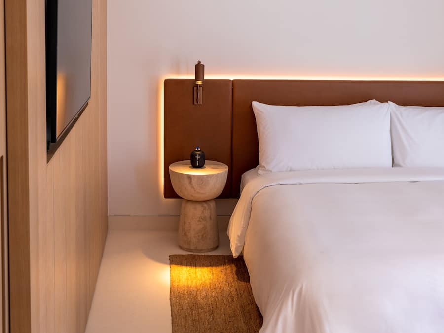 Una habitación de hotel moderna con una cama grande, una mesita de noche, un televisor montado en la pared y una lámpara en una mesita auxiliar.