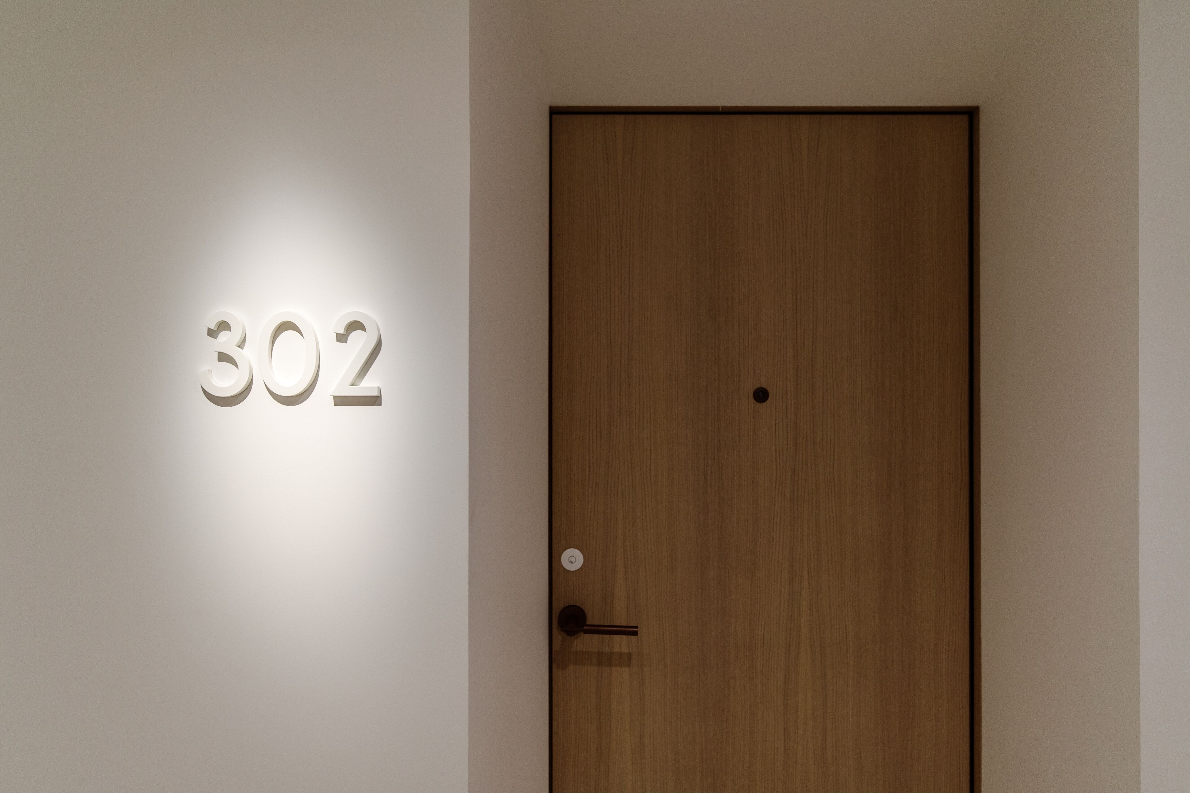 A wooden door with a number '302' illuminated on the wall.