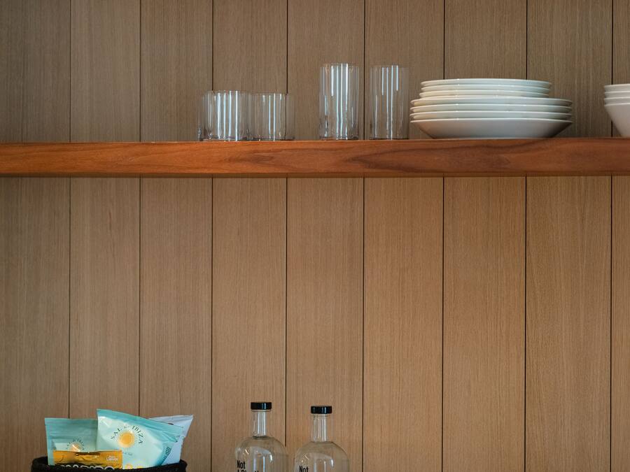Una estantería de madera con vasos transparentes, platos y una cesta que contiene una botella y una bolsa.
