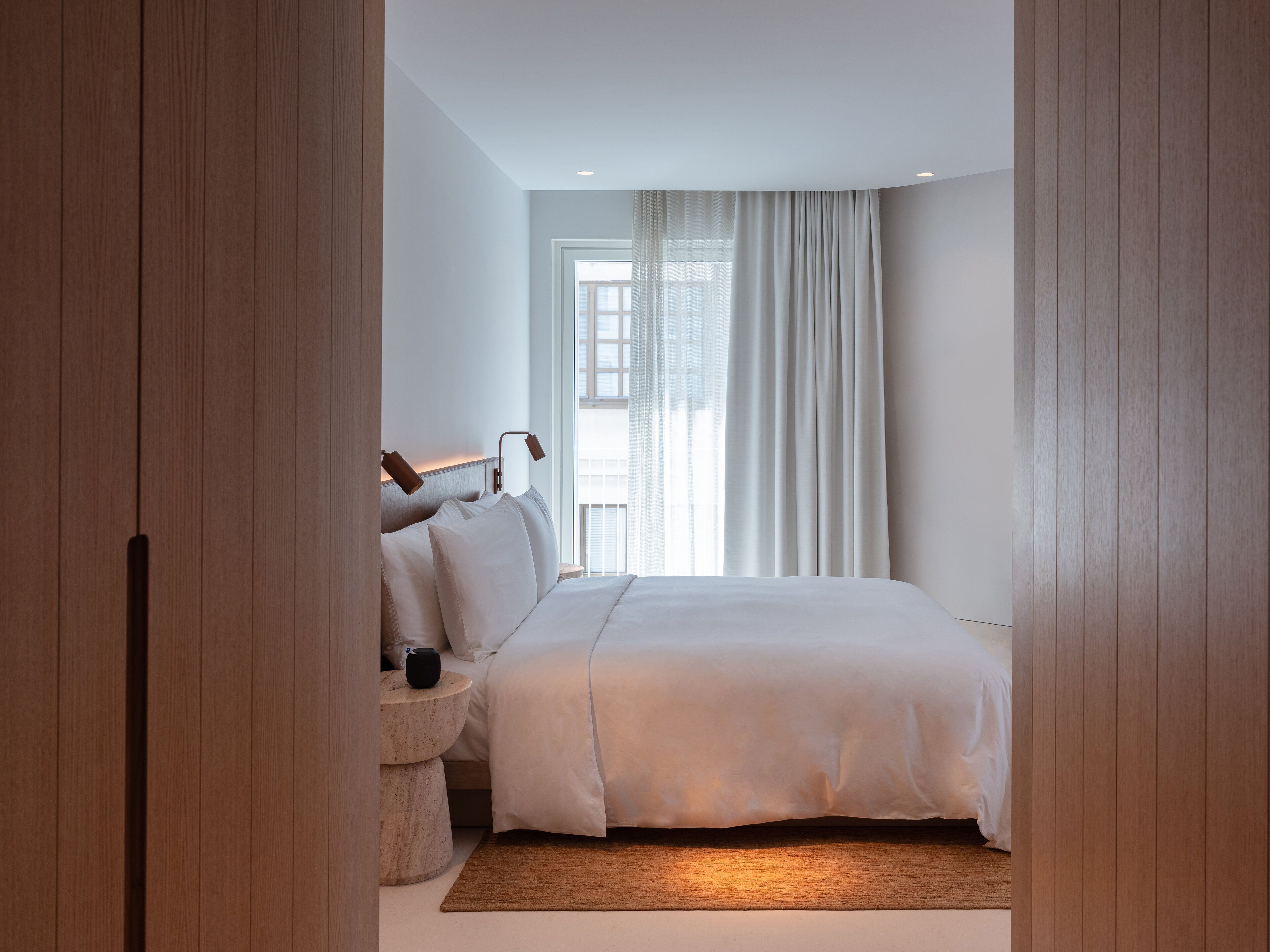 A modern bedroom with a large bed, a bedside table, and a window with curtains.