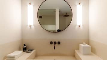 A bathroom with a round mirror, two wall-mounted lights, a sink, a towel, a soap dispenser, and a tissue box.