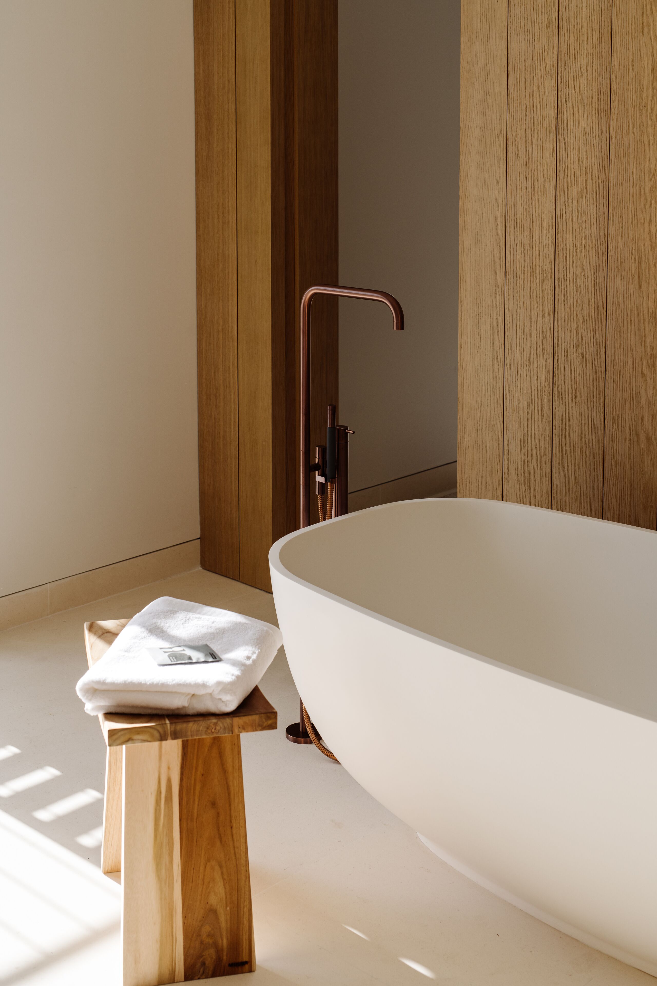Un baño moderno con una bañera independiente, paneles de madera y un taburete de madera con una toalla.