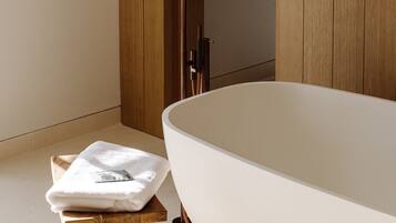Un baño moderno con una bañera independiente, paneles de madera y un taburete de madera con una toalla.