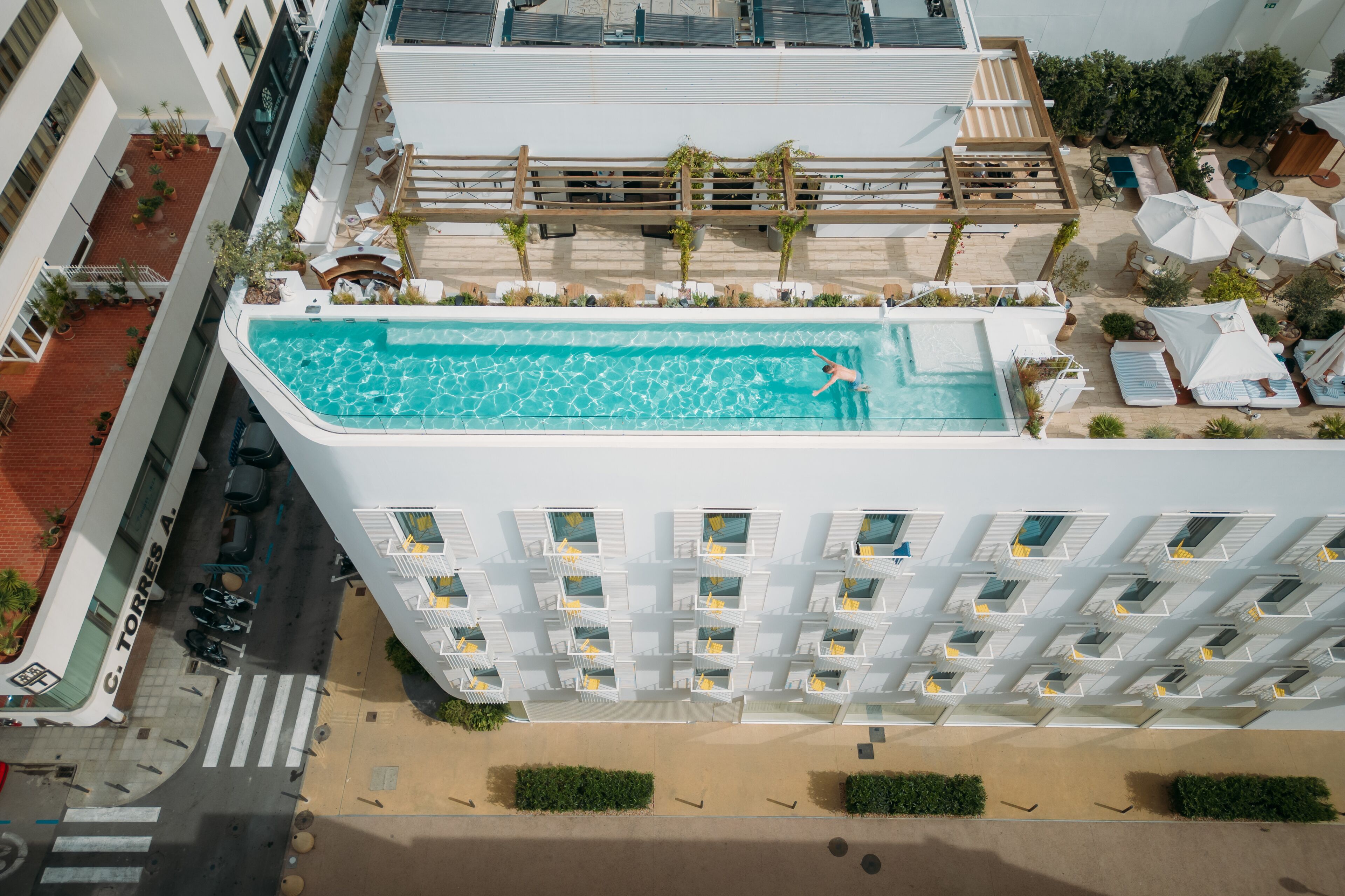A high-rise hotel with a rooftop swimming pool, multiple balconies, and outdoor seating areas.