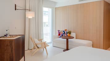 A hotel room with a bed, a wooden desk, a wicker chair, a white sofa, and a small round table.