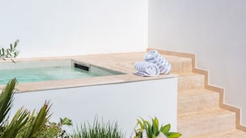 A modern outdoor pool area with a clear blue sky, a small hot tub, and steps leading up to a white building.