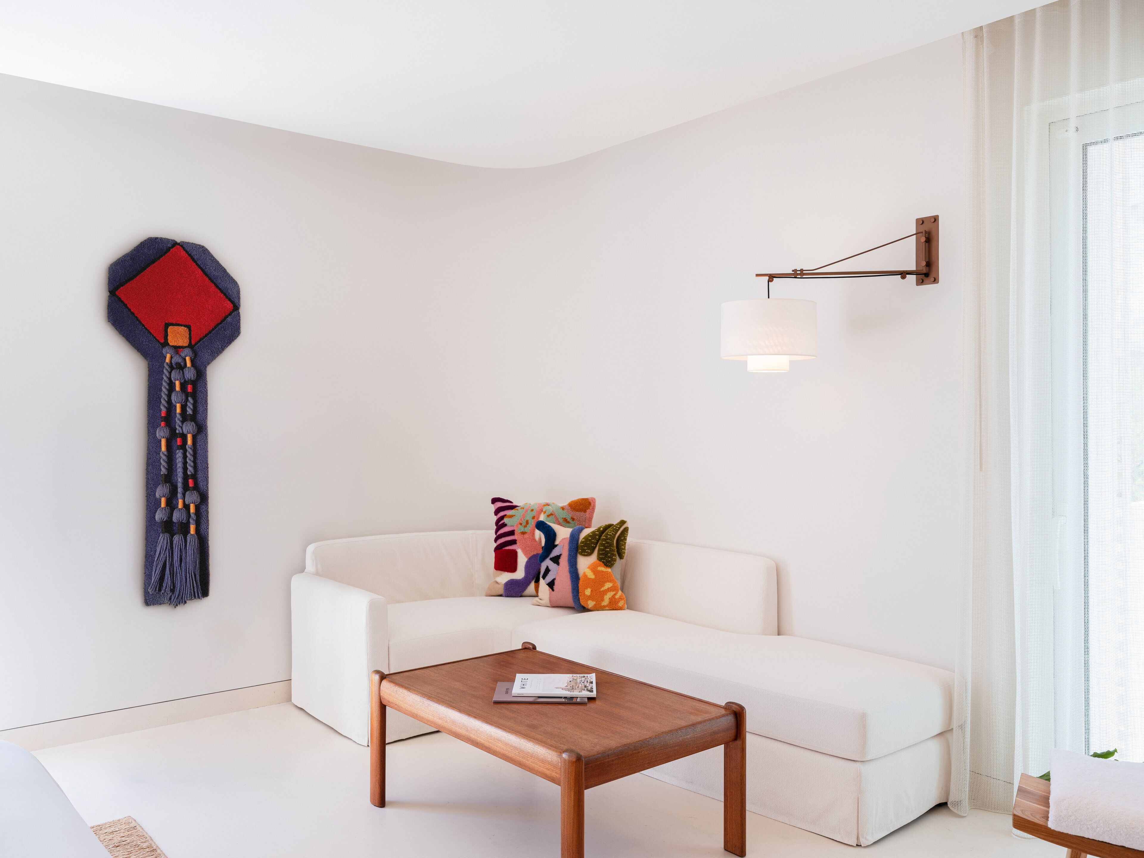 Una sala de estar moderna con un sofá blanco, una mesa de centro de madera y una obra de arte abstracta y colorida en la pared.