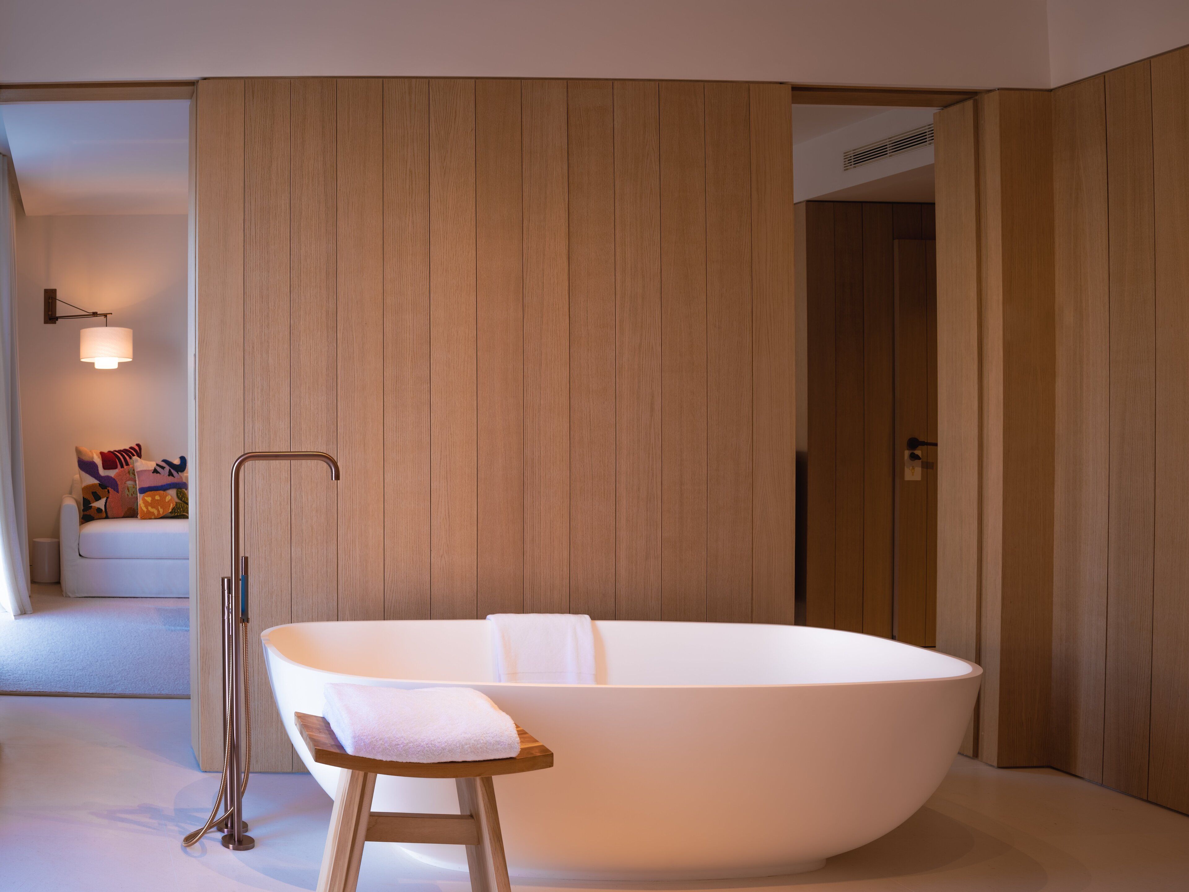 Un baño moderno con una bañera independiente, un banco de madera y una toalla.