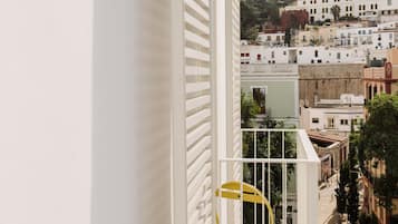 Un balcon doté d’une balustrade blanche et d’une chaise jaune, offrant une vue sur un paysage urbain avec des bâtiments et un ciel dégagé.