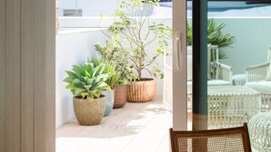 A balcony with potted plants, a wicker chair, and a view of buildings and a body of water. - The Standard, Ibiza (Ibiza Town)