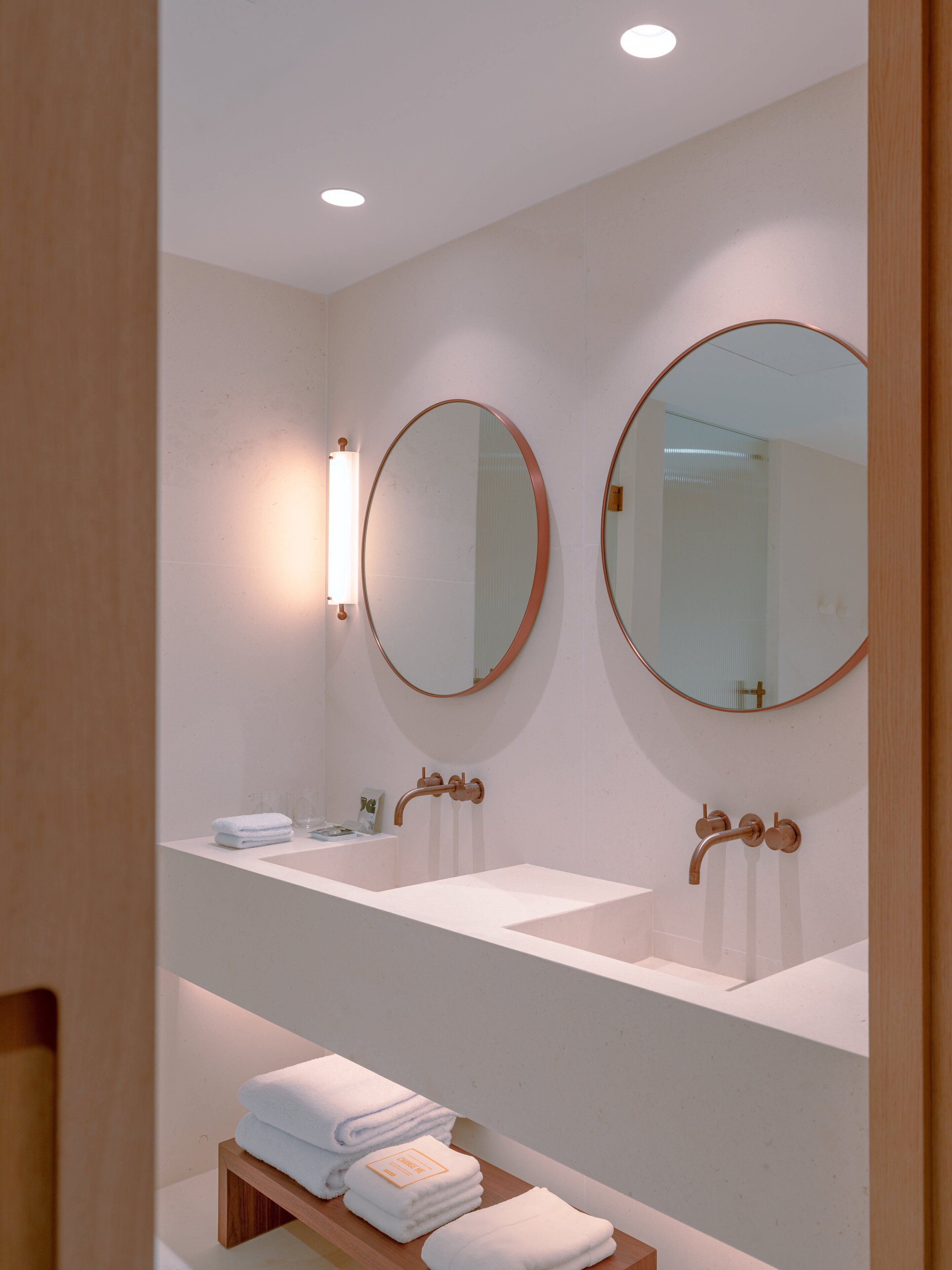 Un baño moderno con dos lavamanos, dos espejos redondos y un estante con toallas dobladas.