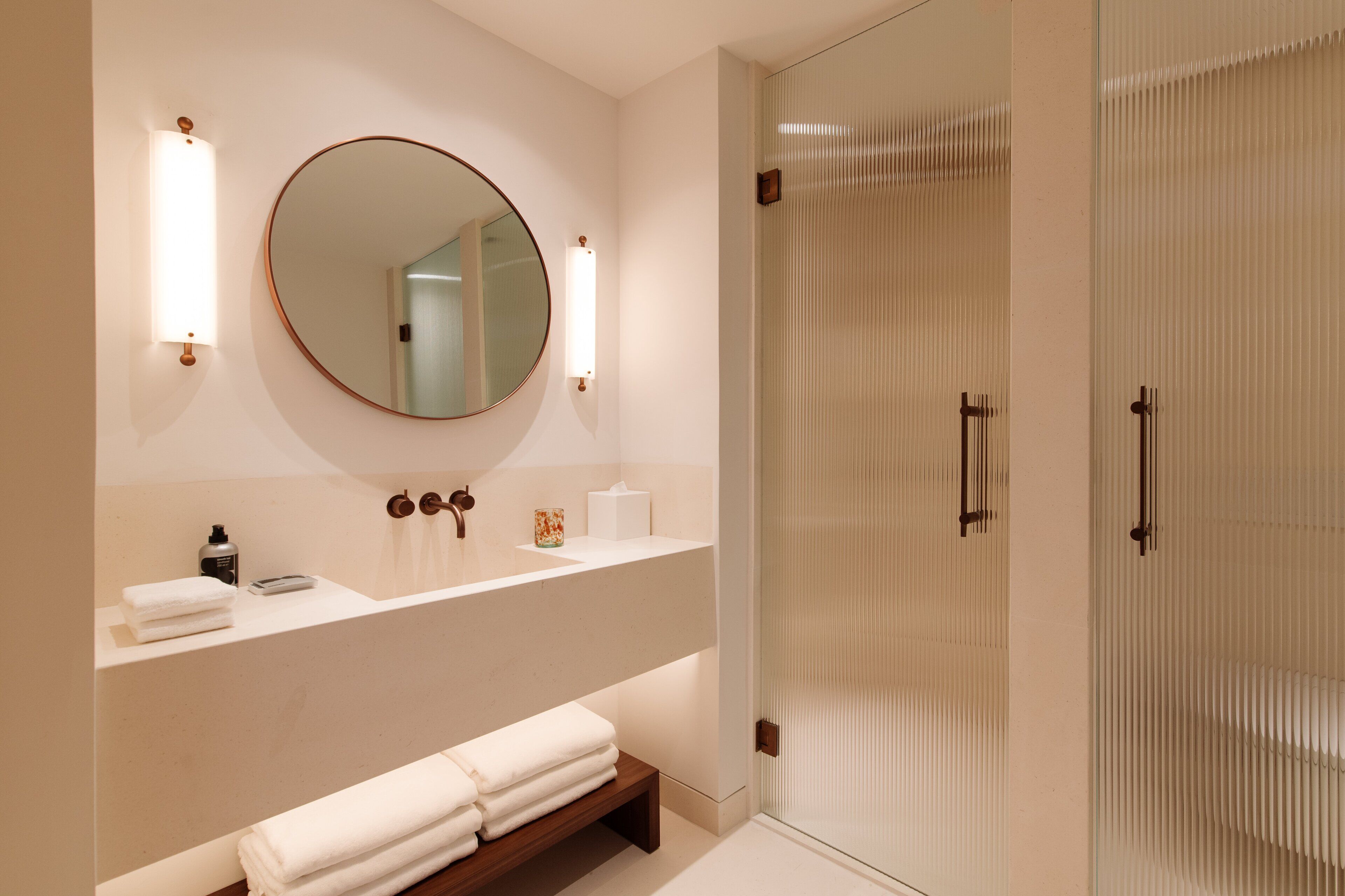 A modern bathroom with a round mirror, two wall-mounted lights, a vanity with a countertop, and a glass shower enclosure.