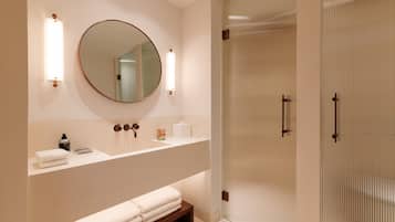 A modern bathroom with a round mirror, two wall-mounted lights, a vanity with a countertop, and a glass shower enclosure.