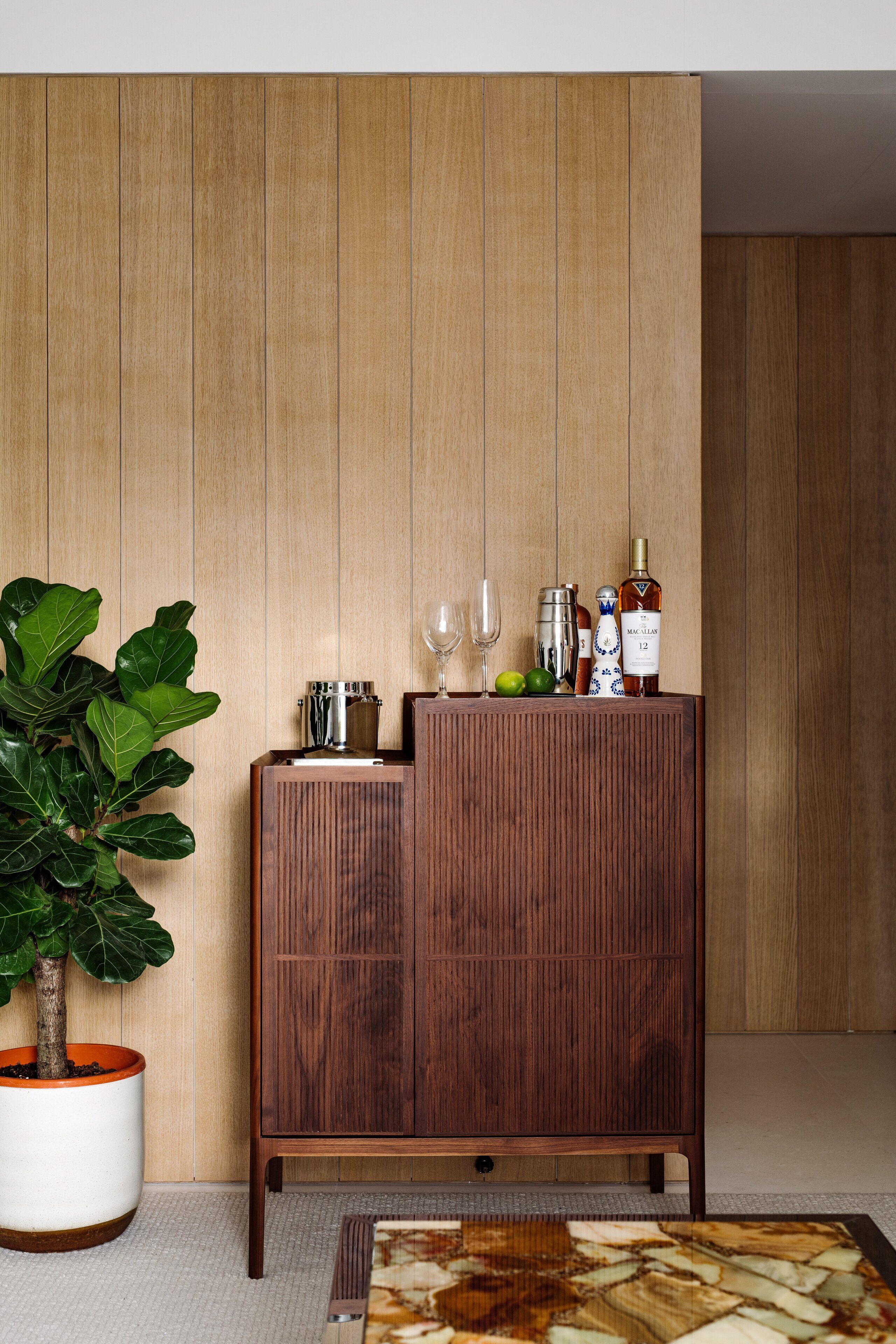Un meuble en bois contenant une bouteille de vin, des verres et une plante.