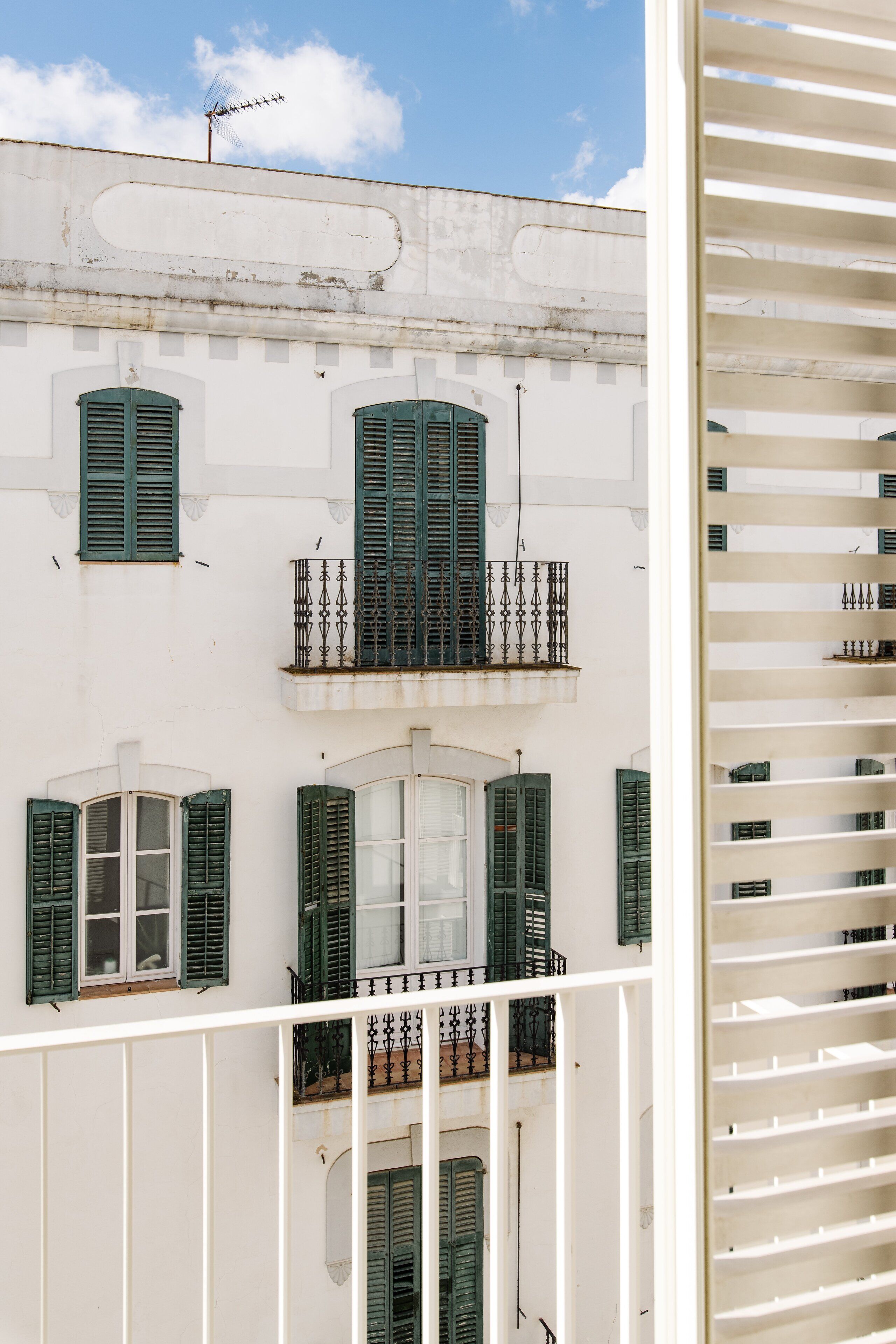 A white building with green shutters and balconies.