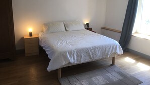 A bedroom with a bed, two bedside tables, a nightstand, a window with curtains, and a wooden floor. - Large bright house with panoramic view (Saizy)